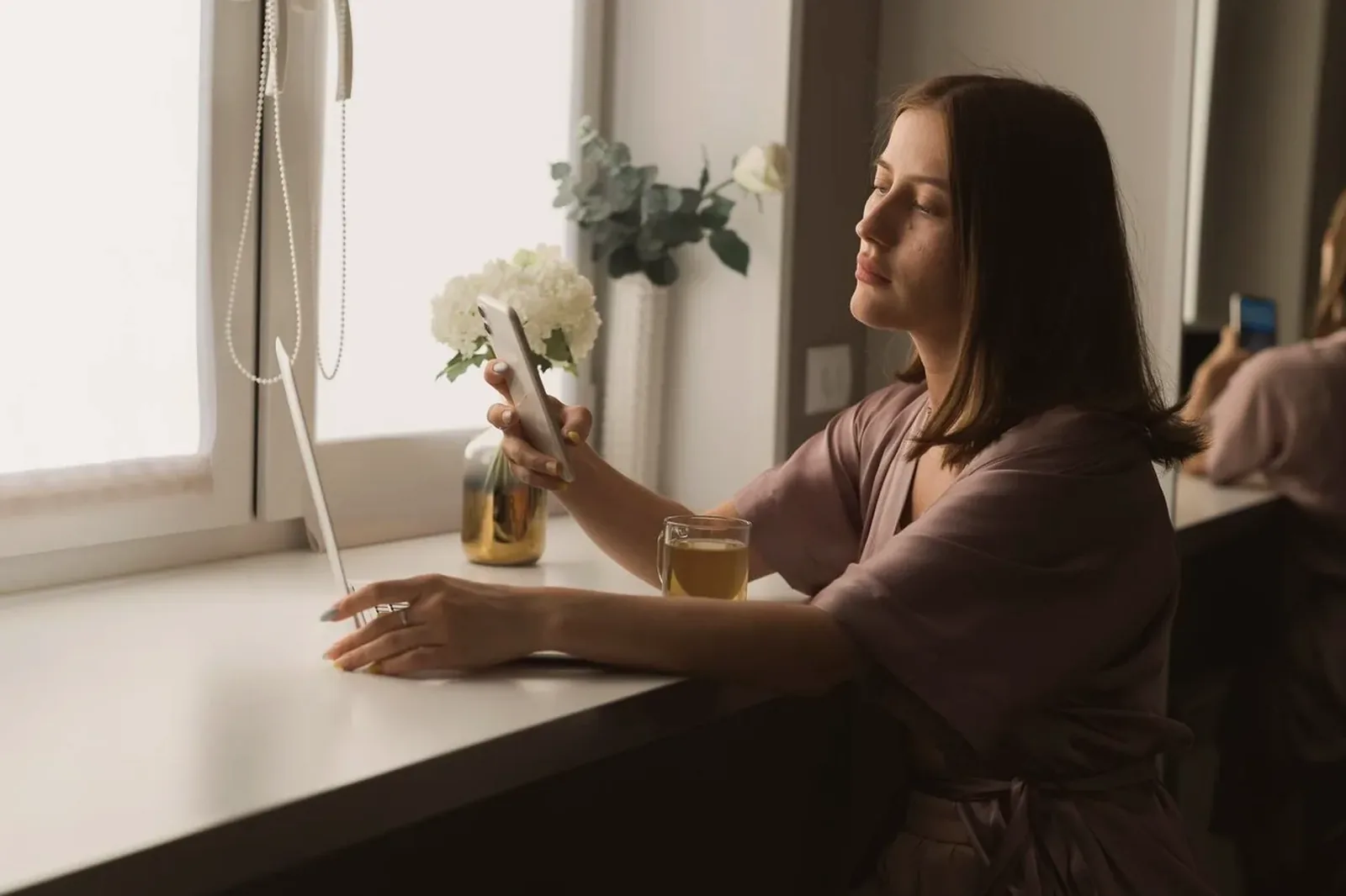A woman sitting by a bright window in a tidy apartment