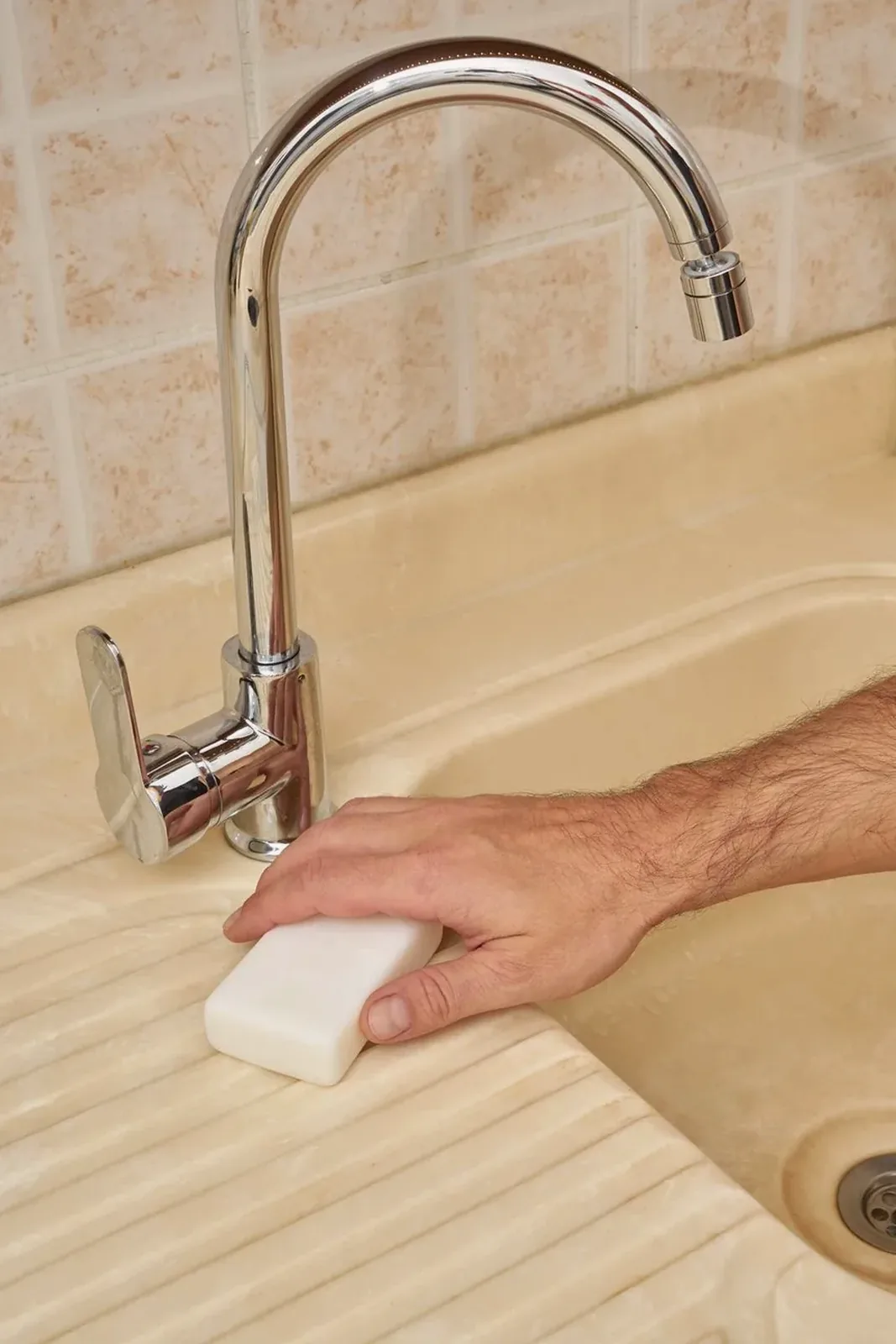 A hand scrubbing a kitchen sink with a sponge